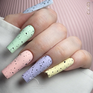 Pose d'ongle multicolore pastel avec finition matte flakes noirs.