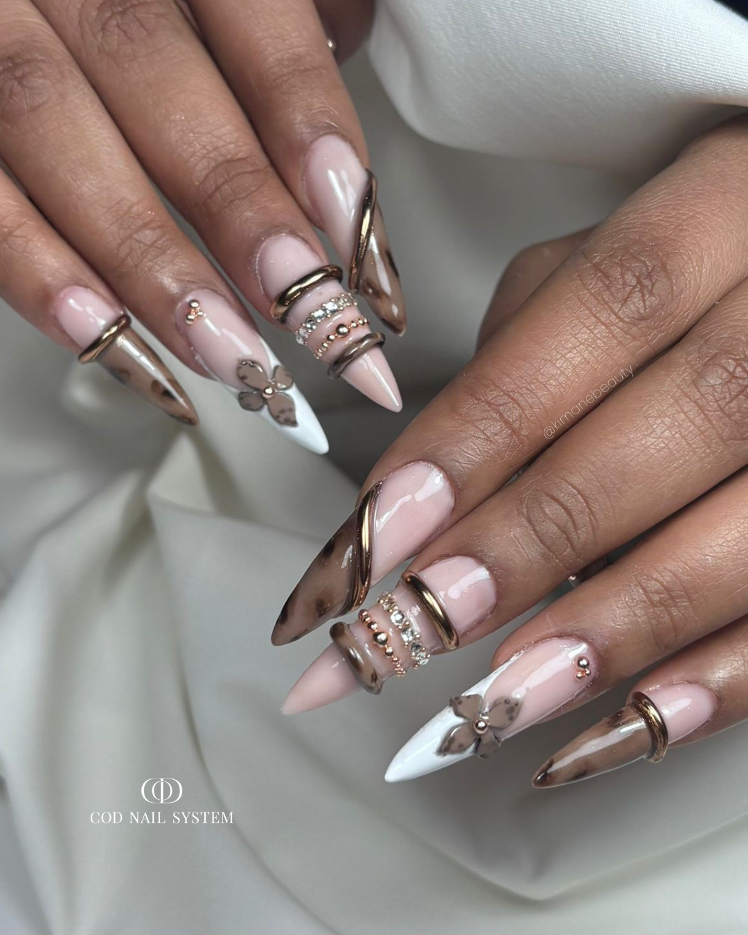 Pose d'ongles stilettos marron avec bague, fleurs 3D et tortoise Pose d'ongles stilettos roses pastels et marron avec bagues et fleurs 3D, effet tortoise et strass
