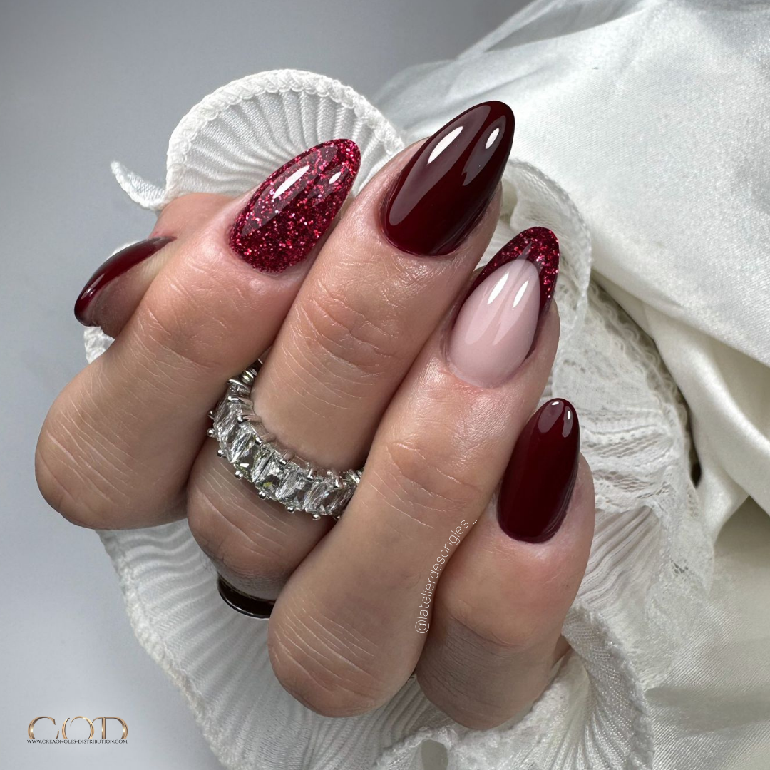 Pose d'ongles en amandes courtes bordeaux avec incrustation de paillettes et french reverse