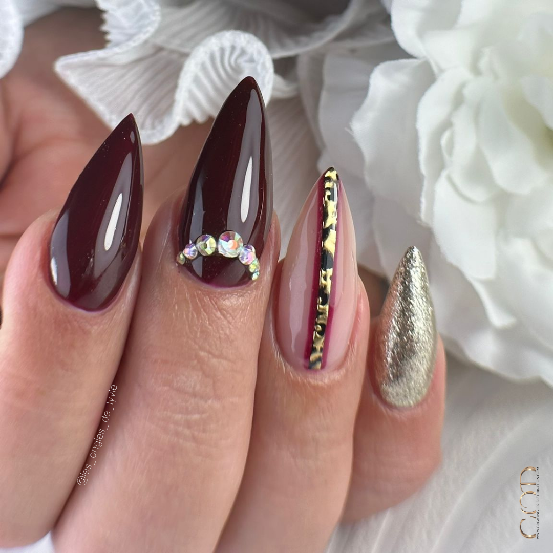 Pose d'ongles stilettos longs bordeaux et doré avec nail art chrome doré et strass