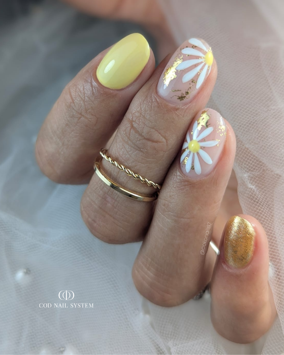 Pose d'ongles ovales courts jaune pastel avec foil doré et nail art fleurs